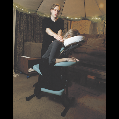 Male therapist massaging neck area of young woman who is seated in a portable massage chair