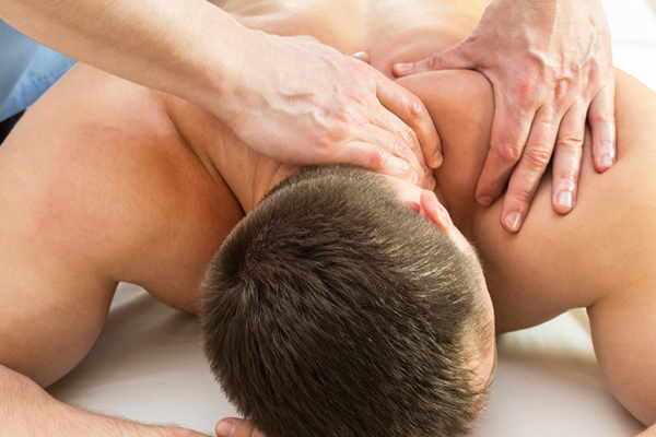 Athletically-built young man lying faced down with male therapist's hands massaging trapezius and neck area