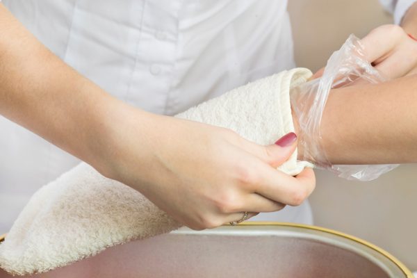 therapist administering paraffin treatment to client's hand; client has thin plastic liner under a snug mitten